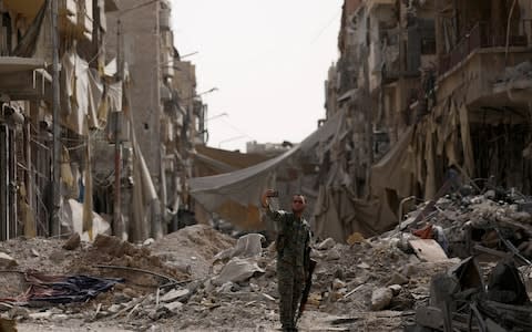 A fighter from Syrian Democratic Forces takes a selfie as he stands near rubble at a damaged site in Raqqa - Credit: Reuters