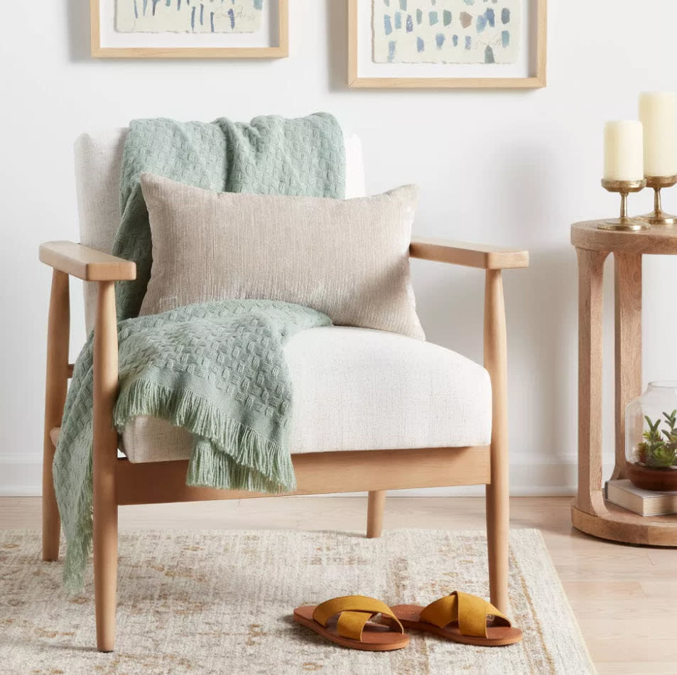 An armchair with cushions and a throw blanket, next to candles, with shoes on the floor