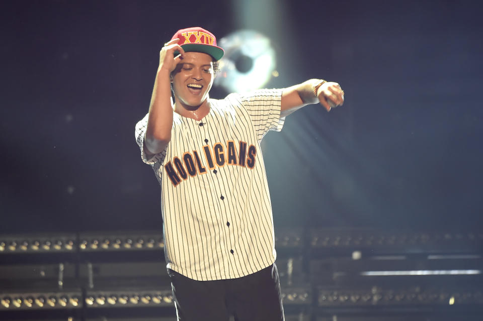 Bruno Mars in a 'Hooligans' baseball jersey and cap, performing on stage with a microphone