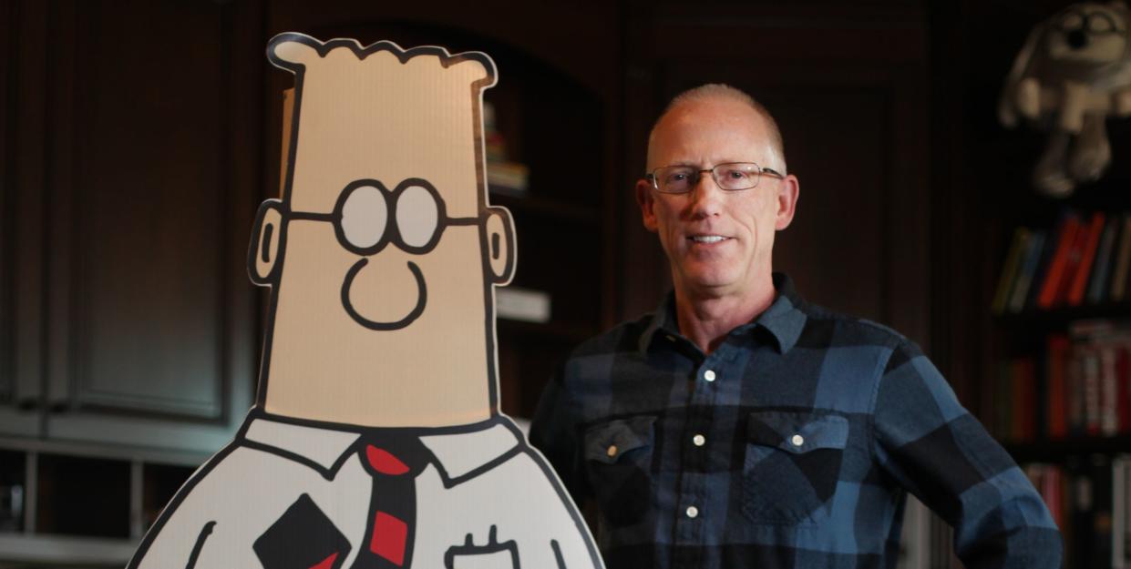 cartoonist scott adams standing with cutout of dilbert comic strip character