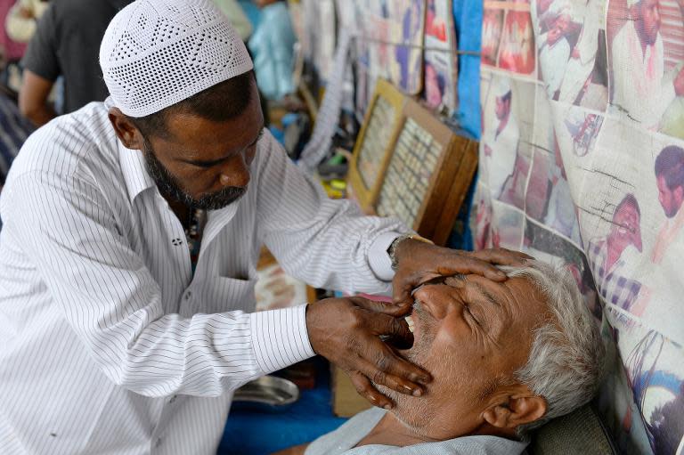 Street dentist Allah Baksh takes measurements for dentures from a customer at his roadside stall at K.R. Market bus stand in Bangalore