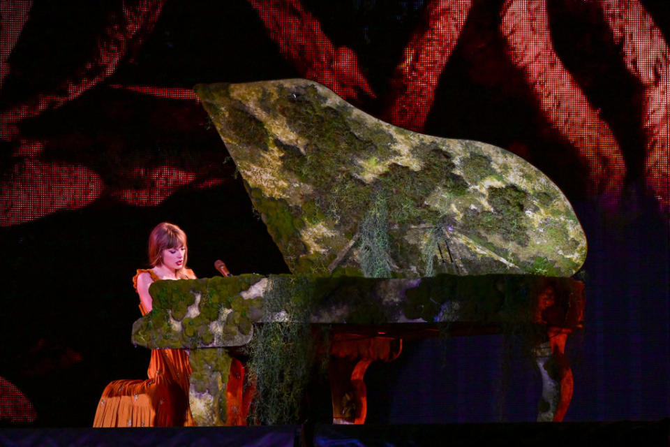 Person playing a moss-covered piano on stage