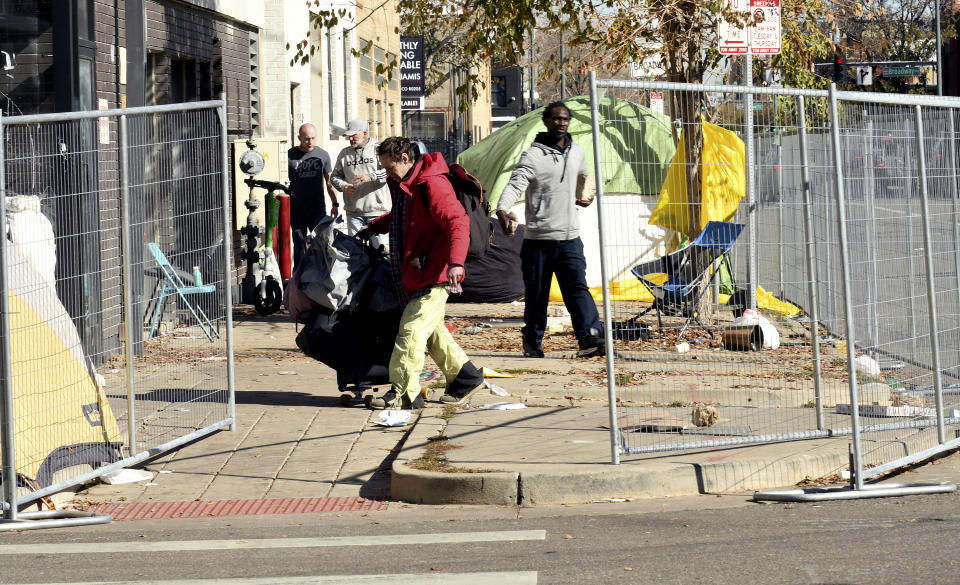 A homeless man moves his belongings during a sweep of an encampment in downtown Denver on Tuesday, Oct. 31, 2023. Crews erected fencing along several blocks near a post office, and police ordered campers to leave. More cities across the U.S. are cracking down on homeless tent encampments that have grown more visible and become unsafe. (AP Photo/Thomas Peipert)