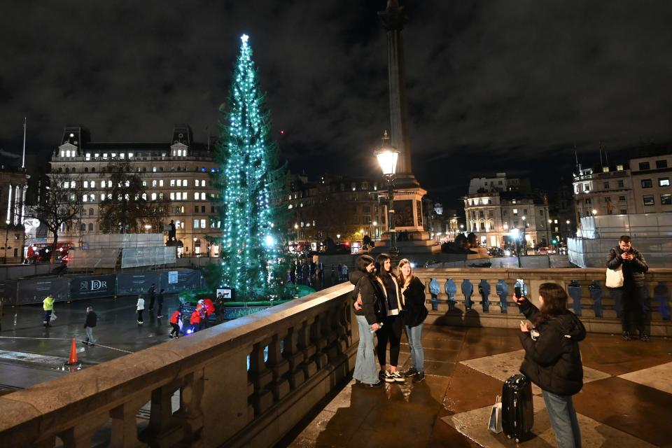 People pose for a photograph in front of the illuminated Christmas tree in Trafalgar Square in central London on December 3, 2020. - The tree is an annual gift to Britain from Norway given as a symbol of friendship and co-operation between the two countries. (Photo by JUSTIN TALLIS / AFP) (Photo by JUSTIN TALLIS/AFP via Getty Images)