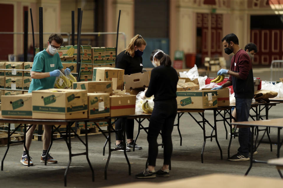 Volunteers for the Edible London food project remove the plastic packaging and check the quality of donated bananas to be put in food packs and delivered to residents who need it in the Haringey Council area, at a hub setup as a result of coronavirus inside the Alexandra Palace venue, in north London, Tuesday, April 21, 2020. The highly contagious COVID-19 coronavirus has impacted on nations around the globe, many imposing self isolation and exercising social distancing when people move from their homes. (AP Photo/Matt Dunham)