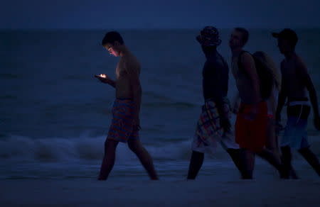 A person looks at his cellphone as he and others walk along the beach at twilight during the Labour Day long weekend in Ft Myers Beach, Florida in this August 31, 2014 file photo. REUTERS/Carlo Allegri/Files