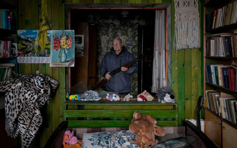 French teacher Pjotr Vyerko, 81, holds a rifle standing behind the broken window of a bedroom in his house   - Vadim Ghirda /AP