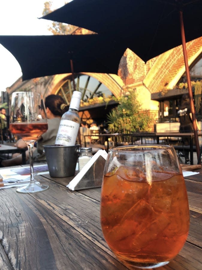 restaurant table with orange cocktail in foreground and bottle in background, salt shaker by the wine