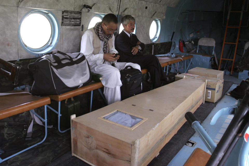 FILE -In this Thursday, Aug. 28, 2008, photo, Japanese doctor Tetsu Nakamura, center right, sits with unidentified man, near the casket of Japanese aid worker Kazuya Ito, who was killed in Nangarhar province, in a helicopter bound for Kabul. The Japanese physician and aid worker in eastern Afghanistan died of his wounds after an attack Wednesday, Dec. 4, 2019, that also killed five Afghans, including the doctor’s bodyguards, the driver and a passenger, a hospital spokesman said. (AP Photo/Rahmat Gul, File)