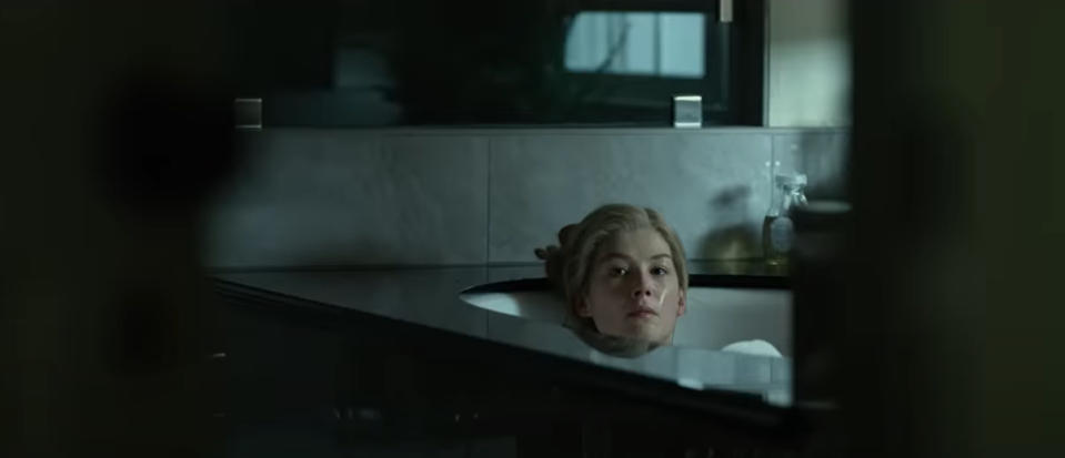 Rosamund Pike as Amy Dunne in Gone Girl is partially submerged in a bathtub, with only her head and shoulders visible above the water. She has a pensive expression.