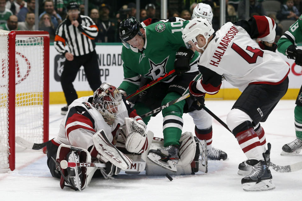 Arizona Coyotes goaltender Adin Hill (31) defends a shot in front of Dallas Stars right wing Corey Perry (10) and Coyotes defenseman Niklas Hjalmarsson (4) during the first period of an NHL hockey game in Dallas, Wednesday, Feb. 19, 2019. (AP Photo/Michael Ainsworth)