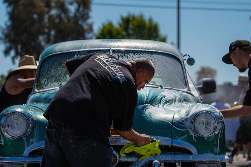 A man leans over to wash the front of a vintage car