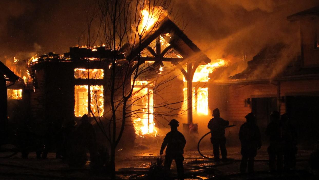 Firemen use a fire hose to try and put out a house fire during a snowfall.