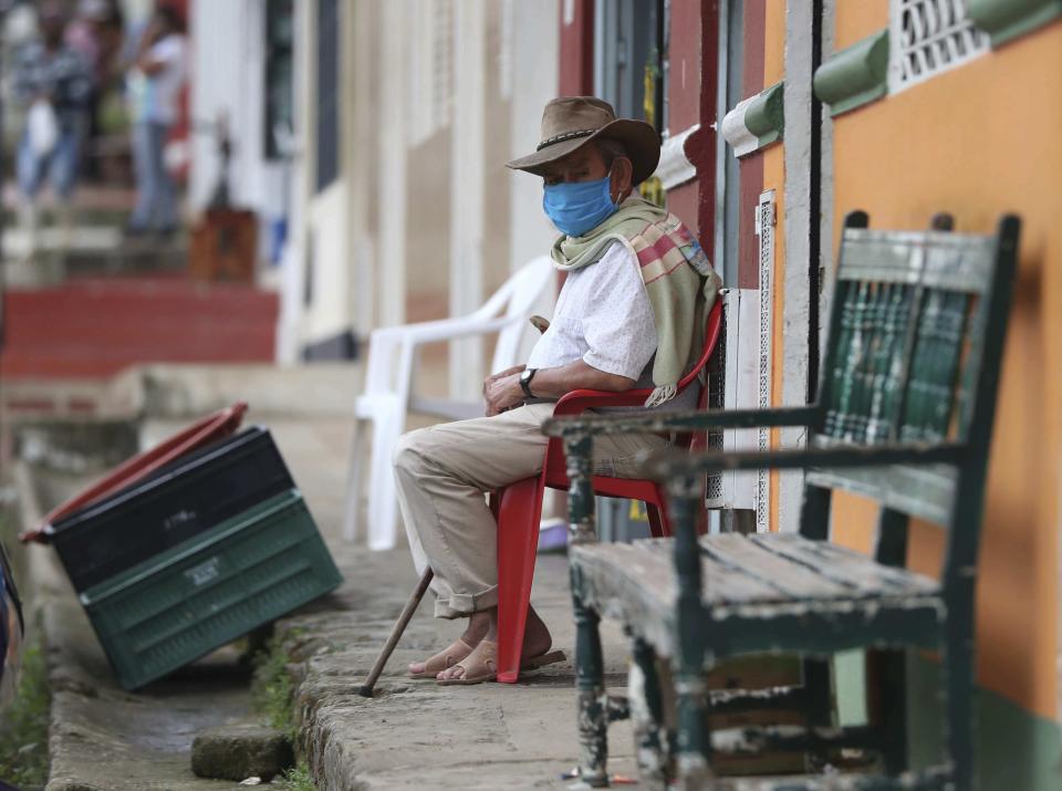 Wearing a mask to curb the spread of the new coronavirus, a man sits on his front porch in Campohermoso, Colombia, Thursday, March 18, 2021. According to the Health Ministry, Campohermoso is one of two municipalities in Colombia that has not had a single case of COVID-19 since the pandemic started one year ago. (AP Photo/Fernando Vergara)