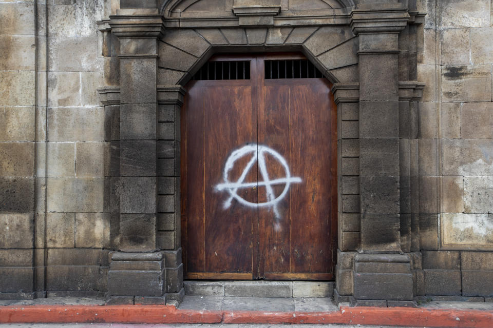 A painted anarchy symbol adorns a door of the Metropolitan Cathedral in Guatemala City, Sunday, Nov. 22, 2020. Protesters also broke into the building and set Congress partially on fire amid growing demonstrations against President Alejandro Giammattei and the legislature for approving a controversial budget that cut educational and health spending. (AP Photo/Moises Castillo)