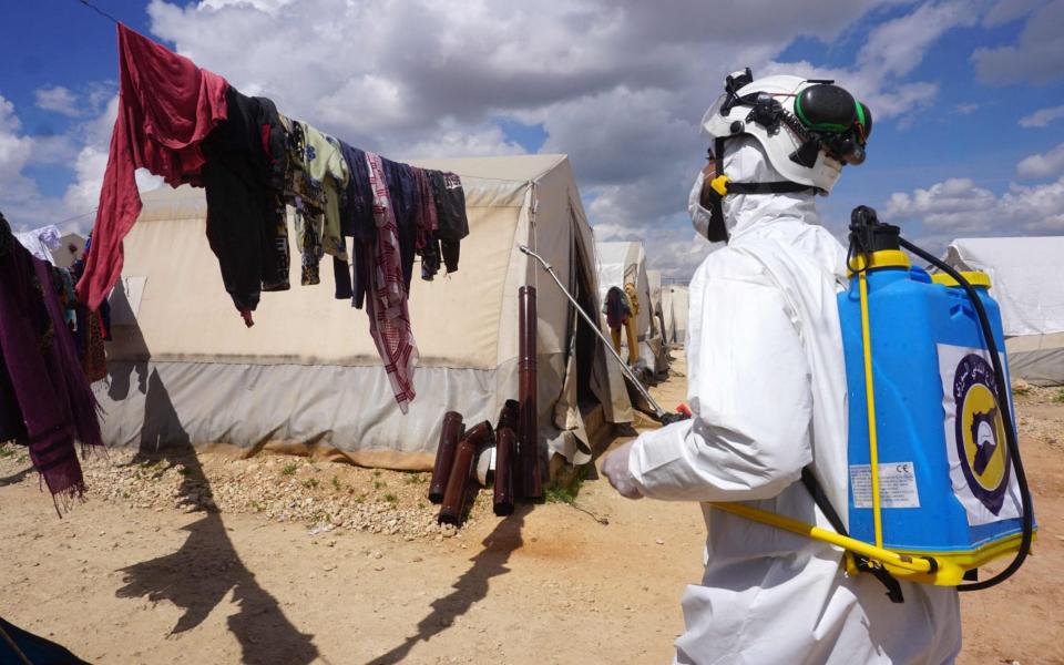 A member of the Syrian civil defence, also known as the White Helmets, sprays disinfectant on washing hanging outside a tent - MUHAMMAD HAJ KADOUR / AFP