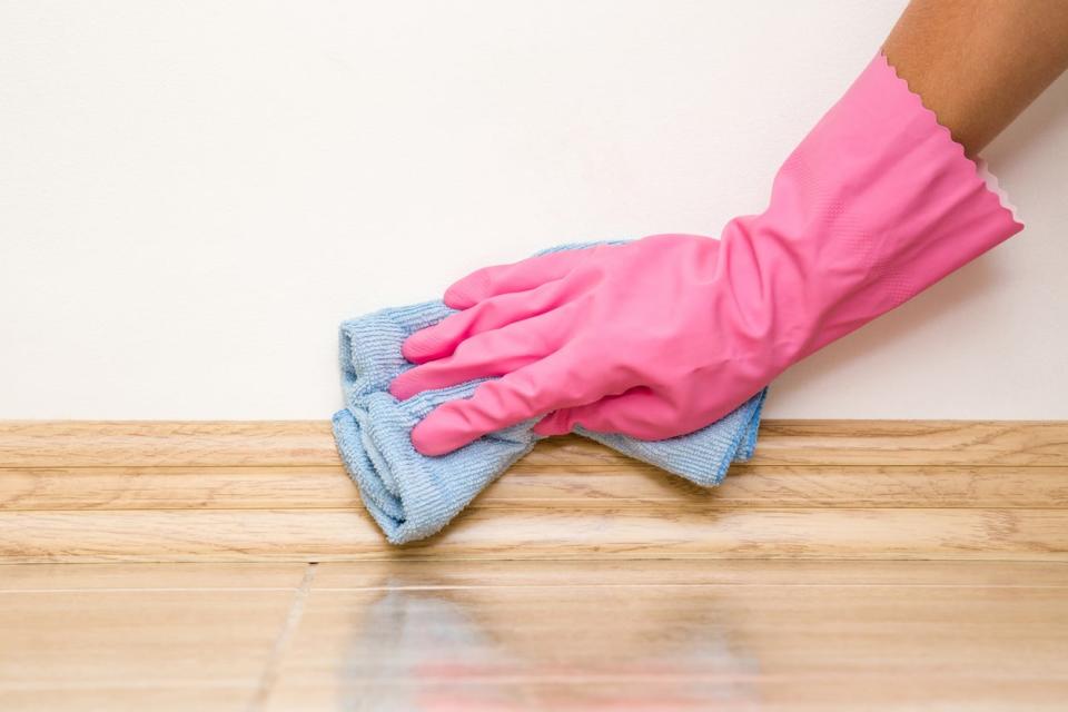 Hand in rubber glove cleaning baseboard with a rag.