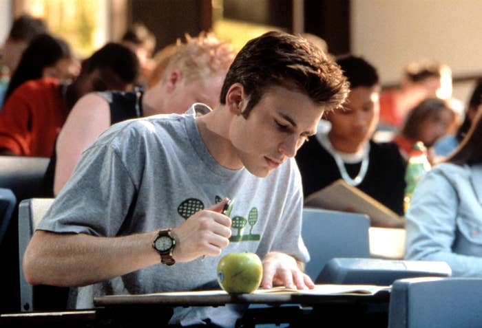 Chris Evans in a classroom setting focused on writing a test, with other students around and an apple on the desk