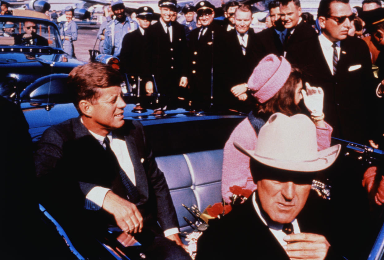 (Original Caption) Texas Governor John Connally adjusts his tie (foreground) as President and Mrs. Jackie Kennedy, in a pink outfit, settled in rear seats, prepared for motorcade into city from airport, Nov. 22. After a few speaking stops, the President was assassinated in the same car.