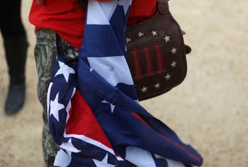 An attendee carries a Confederate flag, a Trump flag and a bag with the III% sign as militia members and pro-gun rights activists participate in the "Declaration of Restoration" rally listen to speakers in Washington, D.C.