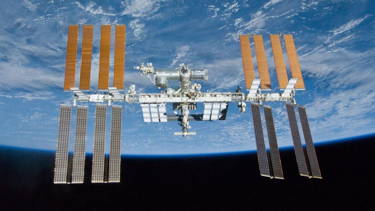  a large space station in the shape of an H floats in front of a blue and white planet 