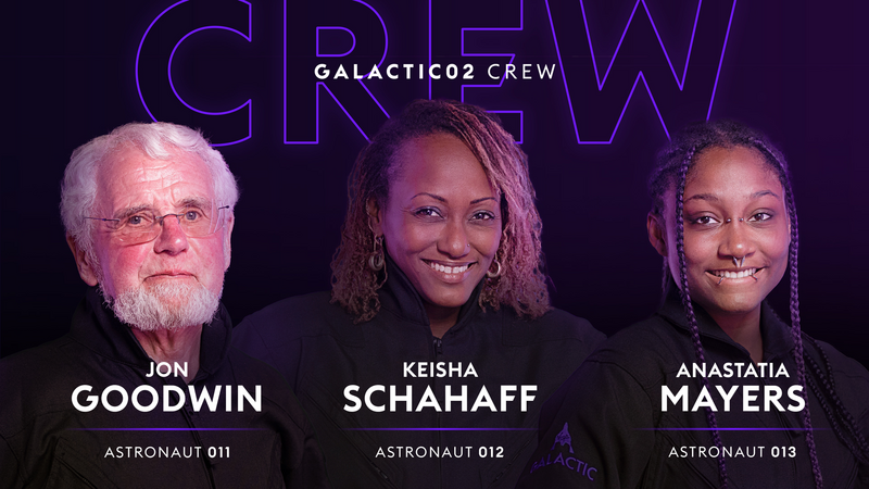  A white, grey-haired man with a beard, a smiling black woman, and a younger smiling black woman with  facial piercings pose for the Galactic02 crew portrait. 