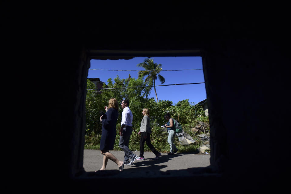 Photographed through an abandoned home, San Juan Mayor Carmen Yulin Cruz Soto, third from left, gives a walking tour to former speaker of the New York City Council Melissa Mark-Viverito, left, and presidential candidate Julian Castro through La Playita, one of the poorest and most affected communities by Hurricane Maria in San Juan, Puerto Rico, Monday Jan. 14, 2019. Castro has joined dozens of high-profile Latinos in Puerto Rico to talk about mobilizing voters ahead of the 2020 elections and increasing Latino political representation to take on President Donald Trump. (AP Photo/Carlos Giusti)