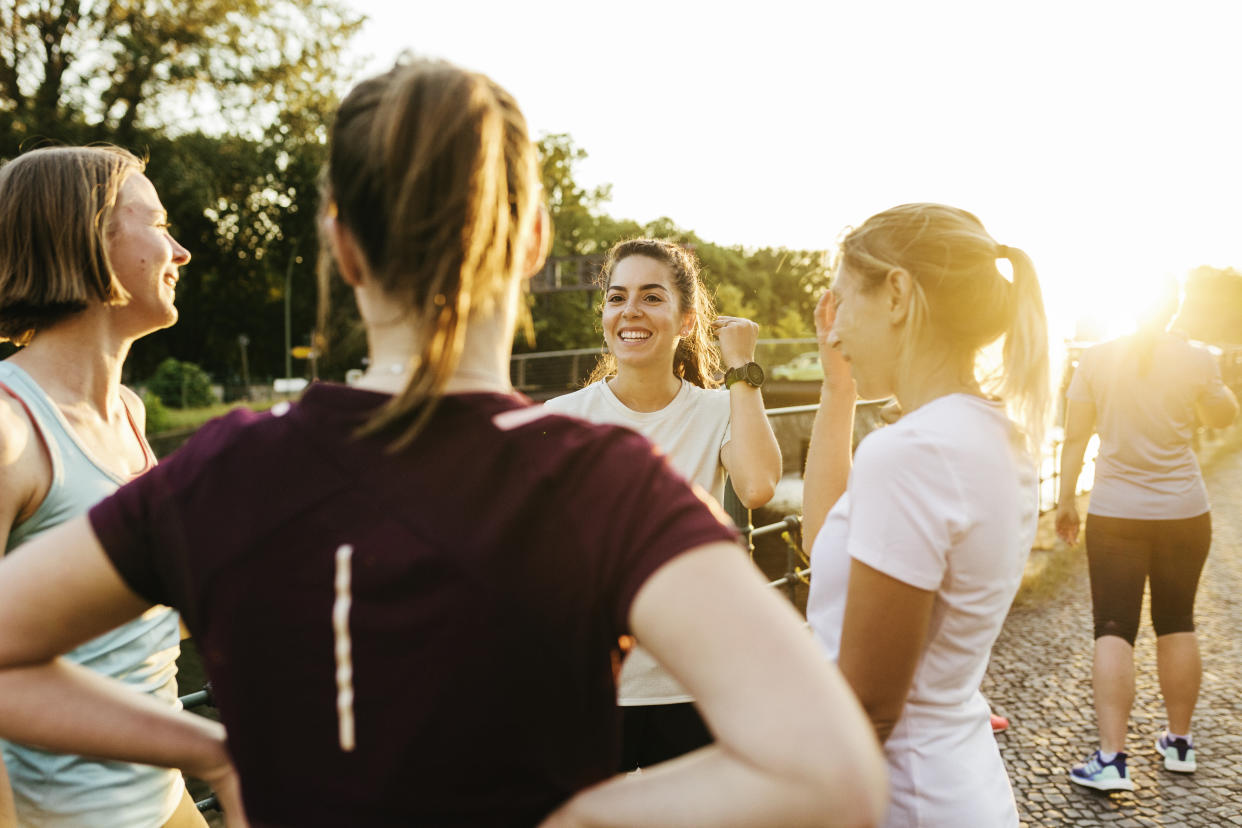 A female fitness group chatting by a canal before beginning a run through the city together.