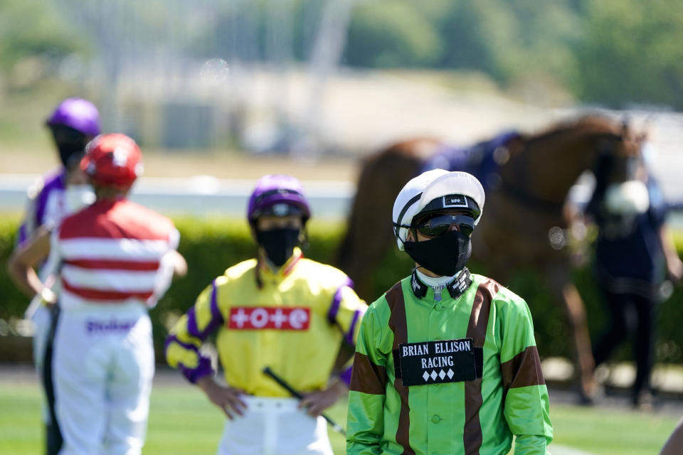 Jockey Ben Robinson wearing a face covering stands with other jockeys as they observe social distancing in the paddock before a race as horse racing is resumed at Newcastle Racecourse, in Newcastle, England, Monday June 1, 2020. Horse Racing in the UK returned to action on Monday, but resuming without spectator racegoers following the coronavirus shutdown. (Alan Crowhurst / PA via AP)