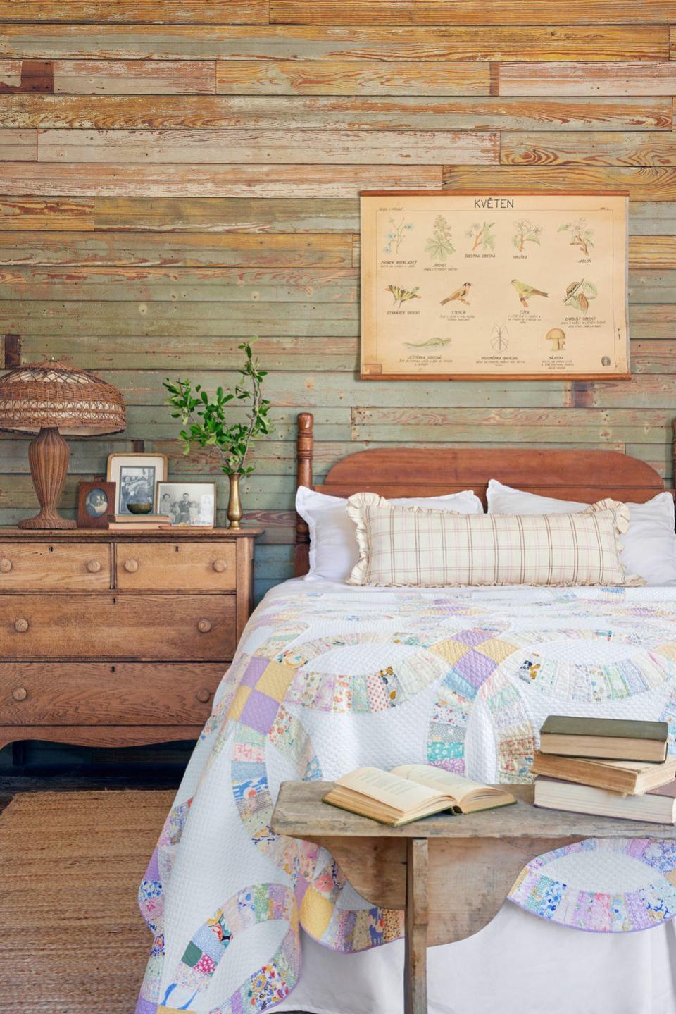 the wall behind the bed is covered in wood salvaged from other parts of a rescued house and the bed is covered with a double wedding ring quilt