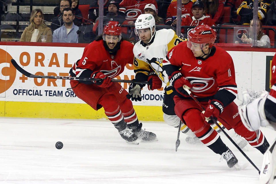 Pittsburgh Penguins Colin White tries to control the puck between Carolina Hurricanes' Jalen Chatfield (5) and Jack Drury (18) during the first period of an NHL hockey game in Raleigh, N.C., Saturday, Jan. 13, 2024. (AP Photo/Karl B DeBlaker)