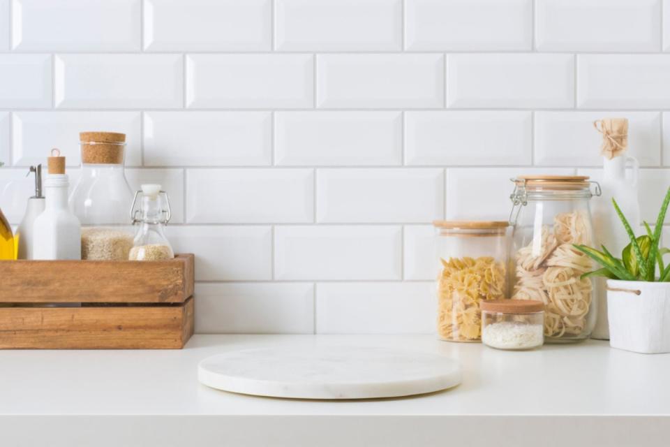 A close up of white tile kitchen backsplash with jars in front.