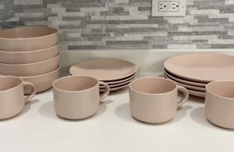 Reviewer's photo of the set of stoneware dishes in the color blush pink, stacked and lined up on a kitchen counter