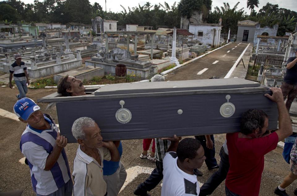 In this Feb. 5, 2014 photo, Divaldo Aguiar, who plays the part of Pachencho, is carried in a mock coffin during the Burial of Pachencho celebration, through a cemetery in Santiago de Las Vegas, Cuba. Cuban villagers stage a mock funeral and burial of Pachencho, with a living man playing the part of Pachencho, in a boozy festival that has become an annual tradition in this small town near Havana, held each Feb. 5 for the last 30 years. (AP Photo/Enric Marti)