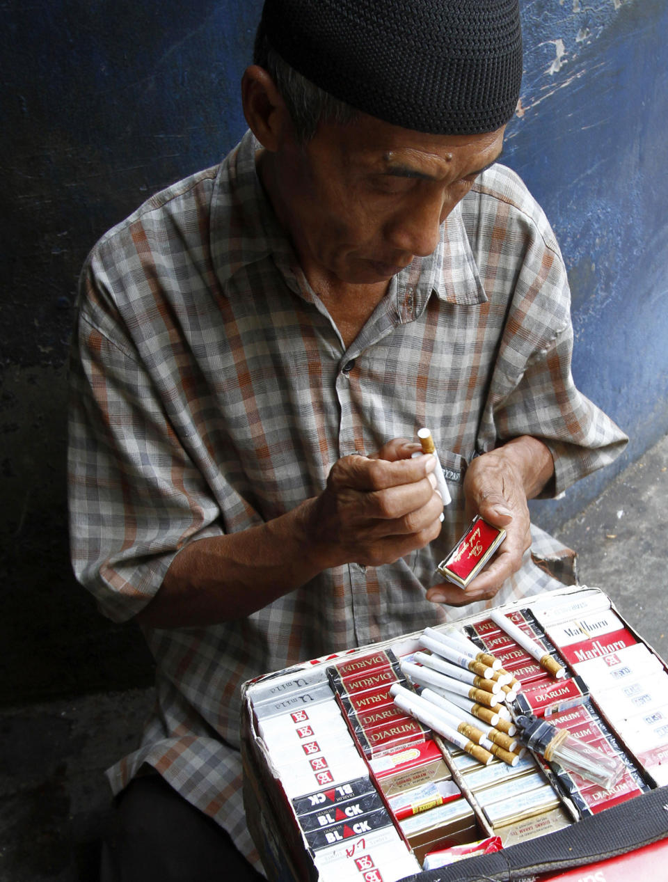 A cigarette vendor packs cigarettes to be sold individually for one US cent per stick in Jakarta, Indonesia, Tuesday, Sept. 11, 2012. Indonesian men rank as the world’s top smokers, with two out of three of them lighting up in a country where cigarettes cost pennies and tobacco advertising is everywhere. (AP Photo/Achmad Ibrahim)