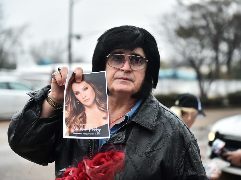 A fan dressed as Elvis holds a program for Lisa Marie Presley's memorial service.