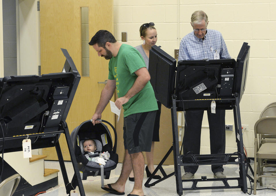 Tiger Outterson hangs on to five-month-old Cruise Outterson while Jessica Outterson prepares to vote with the help of William MacDonald Precinct #74 equipment supervisor at Alexander Graham Middle School in south Charlotte, N.C., where voters could cast their ballots in the party primaries and also could vote on the 9th District race between Dan Bishop and Dan McCready. (John D. Simmons/The Charlotte Observer via AP)