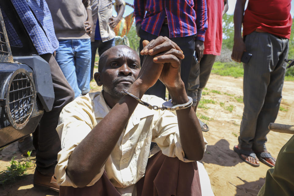 An unidentified man sits in handcuffs after being arrested accused of having connections with pastor Paul Makenzi, in a forest near the village of Shakahola, near the coastal city of Malindi, in southern Kenya Monday, April 24, 2023. Kenya's president William Ruto said Monday that the starvation deaths of dozens of followers of pastor Paul Makenzi, who was arrested on suspicion of telling his followers to fast to death in order to meet Jesus, is akin to terrorism. (AP Photo)