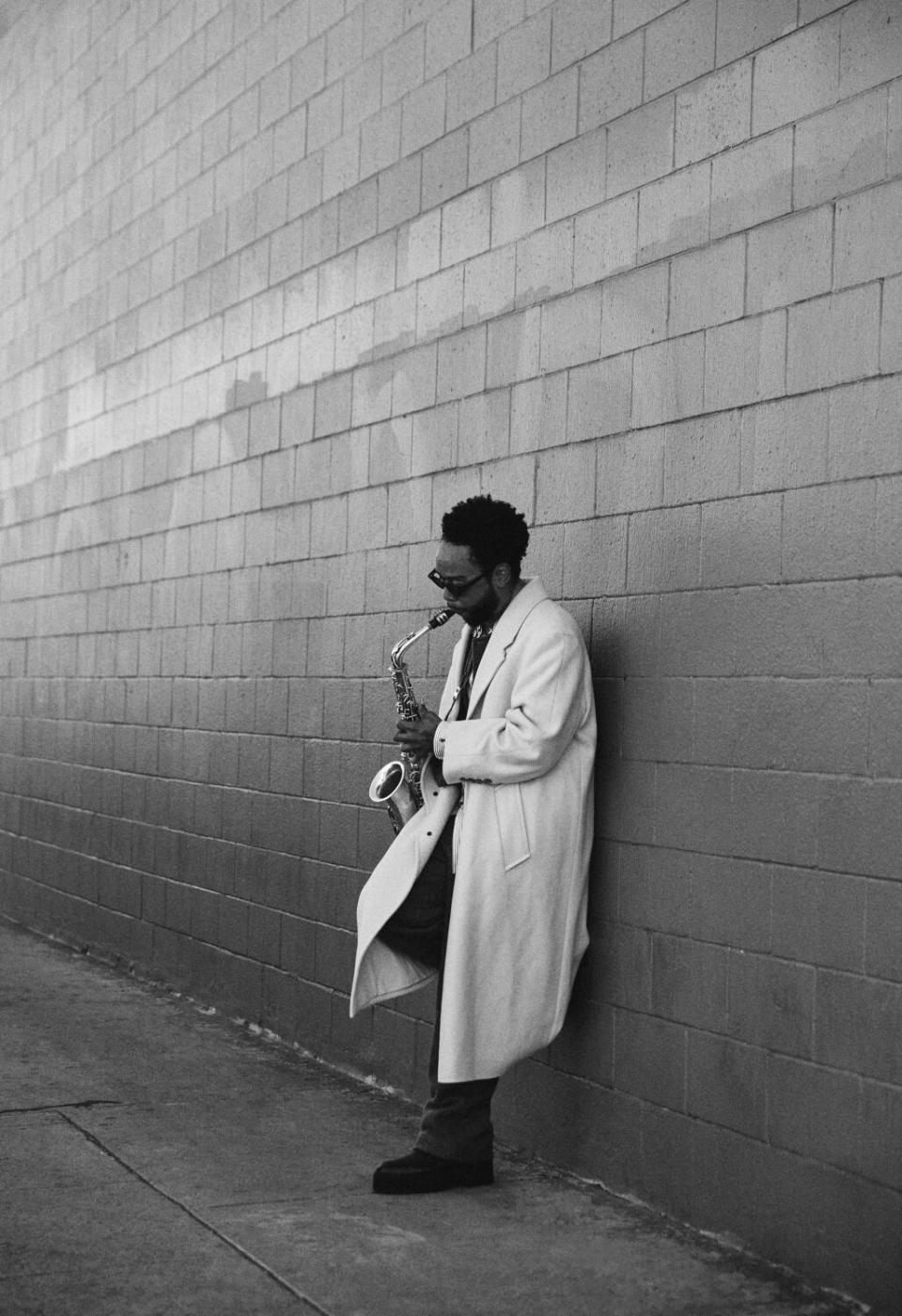 Terrace Martin plays the saxophone as he leans against a cement-block wall in a black-and-white photo.