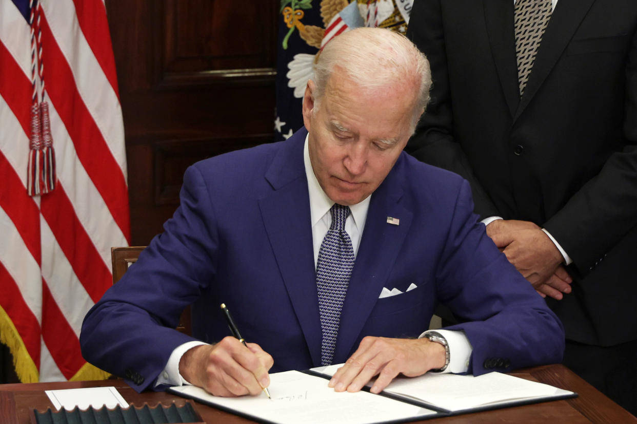 President Biden, seated at a desk next to an American flag, signs an executive order.