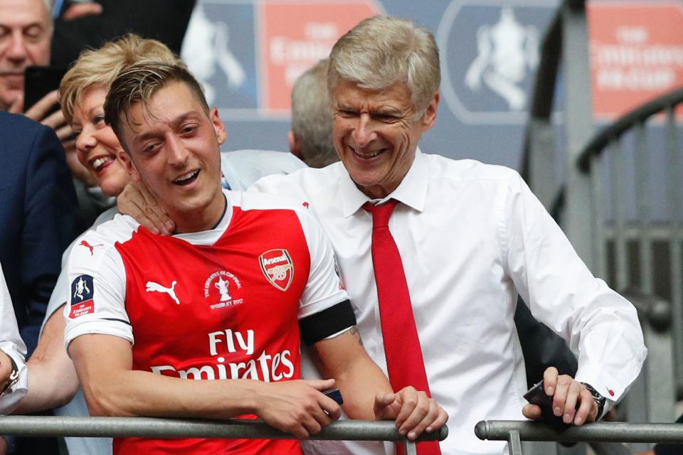 Arsenal's French manager Arsene Wenger (R) and Arsenal's German midfielder Mesut Ozil smile as Arsenal players celebrate their victory over Chelsea in the English FA Cup final football match between Arsenal and Chelsea at Wembley stadium in London on May 27, 2017. Aaron Ramsey scored a 79th-minute header to earn Arsenal a stunning 2-1 win over Double-chasing Chelsea on Saturday and deliver embattled manager Arsene Wenger a record seventh FA Cup. / AFP PHOTO / Adrian DENNIS / NOT FOR MARKETING OR ADVERTISING USE / RESTRICTED TO EDITORIAL USE        (Photo credit should read ADRIAN DENNIS/AFP/Getty Images)