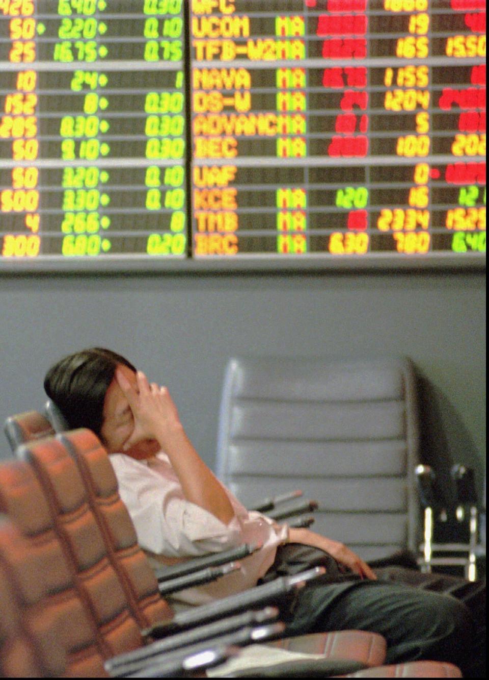 FILE- In this Nov. 21, 1997, file photo a Thai stock investor falls asleep while lonely monitoring a trading board at a stock house in the Stock Exchange of Thailand in Bangkok. A financial crisis that began in 1997 after Thailand devalued its currency against the U.S. dollar eventually sent markets reeling across the region in what became known as the Asian financial crisis. (AP Photo/Thaksina Khaikaew, File)