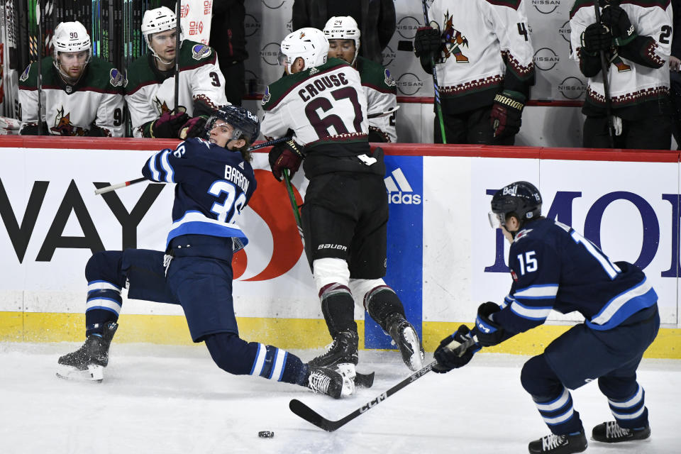 Arizona Coyotes left wing Lawson Crouse (67) and Winnipeg Jets center Morgan Barron (36) collide along the boards as Winnipeg Jets center Rasmus Kupari (15) picks up the loose puck during the first period of an NHL hockey game in Winnipeg, Manitoba on Sunday, Feb. 25, 2024. (Fred Greenslade/The Canadian Press via AP)