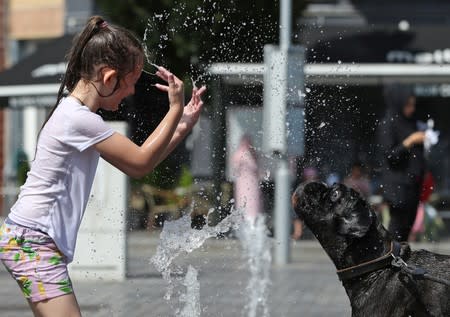 A girl plays with her dog in a water fountain on a hot summer day in Brussels