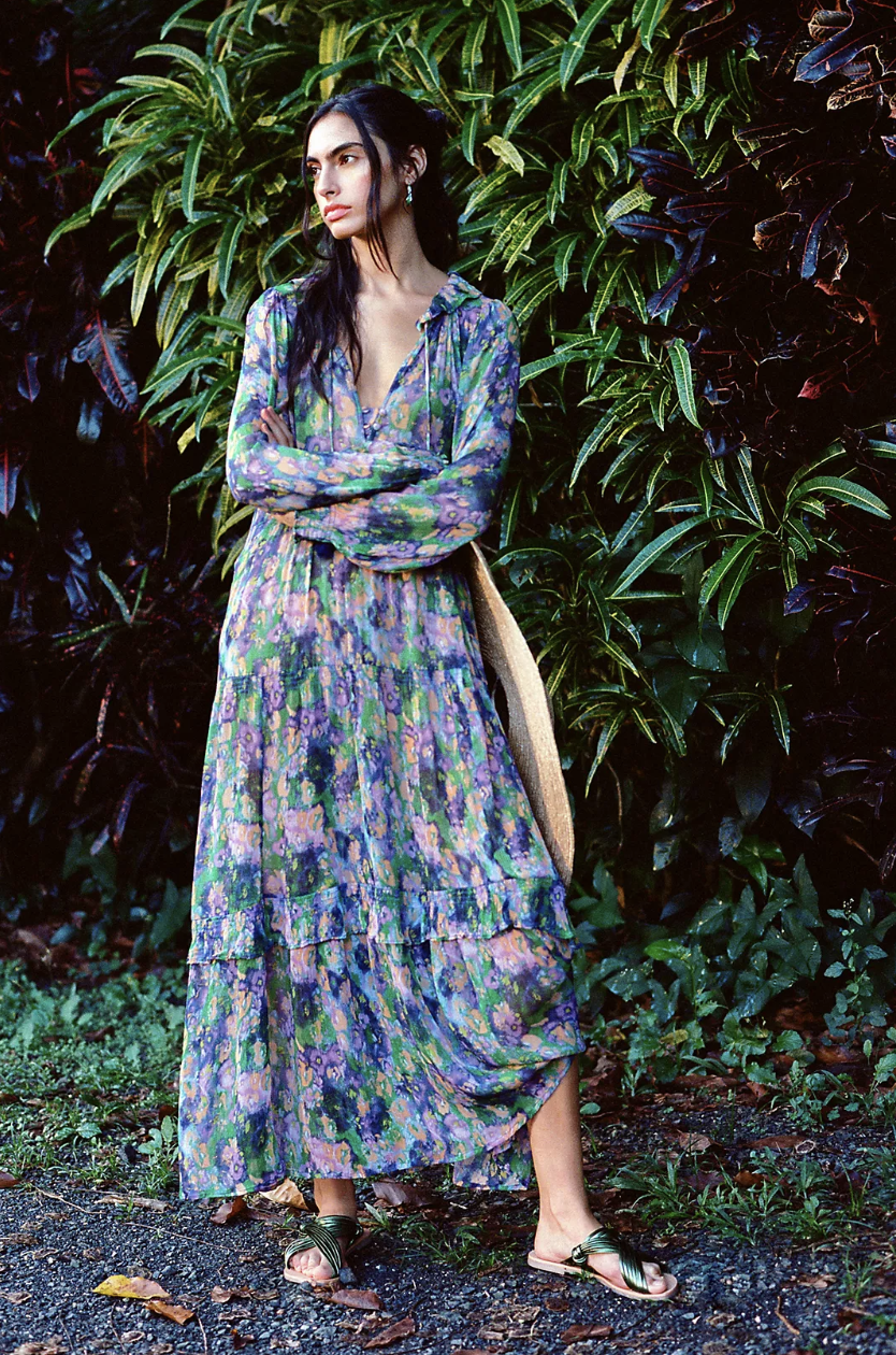 woman standing against green tree in purple and green The Marais Printed Chiffon Maxi Dress (photo via Anthropologie)