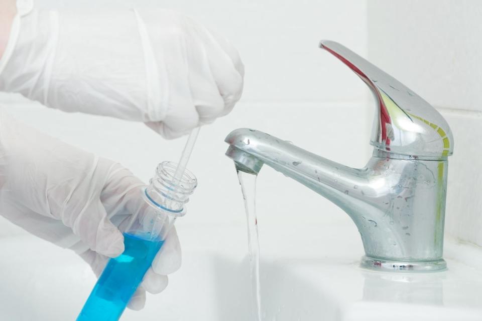 A gloved person testing the water from a bathroom sink faucet.