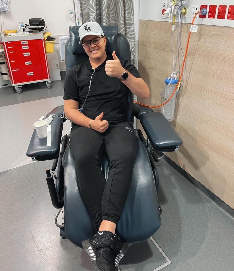 Former Home & Away star Johnny Ruffo gives a thumbs up while receiving chemotherapy from a blue hospital chair during his second brain cancer battle