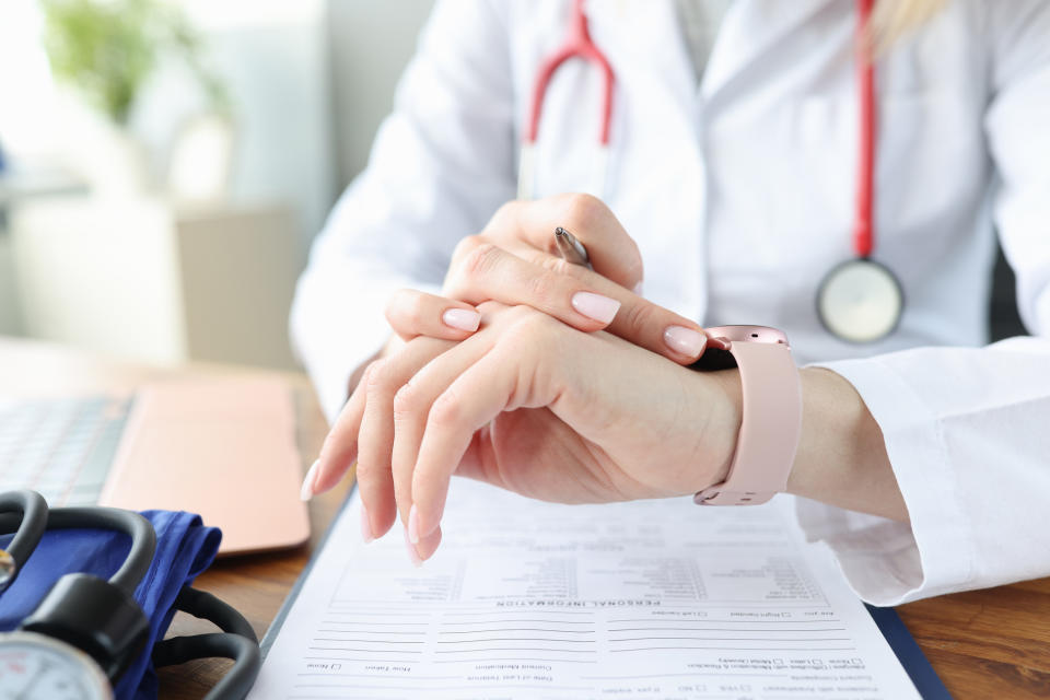 Doctor with stethoscope clasped hands over a medical document on desk