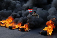 FILE- An anti-government demonstrator holds a national flag and runs across tires that were set on fire to block a main highway during a protest against a ruling elite they say has failed to address the economy's downward spiral, in the town of Jal el-Dib, north of Beirut, Lebanon, Tuesday, Jan. 14, 2020. Lebanon and Sri Lanka may be a world apart, but they share a history of political turmoil and violence that led to the collapse of once-prosperous economies bedeviled by corruption, patronage, nepotism and incompetence. (AP Photo/Bilal Hussein, File)