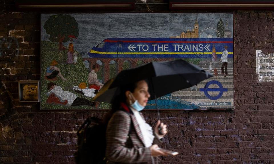 A woman with an umbrella walking past a mosaic sign saying 